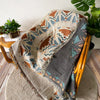 A woven throw blanket featuring a bohemian jacquard pattern in earthy tones of brown, teal, and beige.