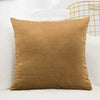 A solid velvet decorative cushion cover in a warm brown color resting on a white surface.