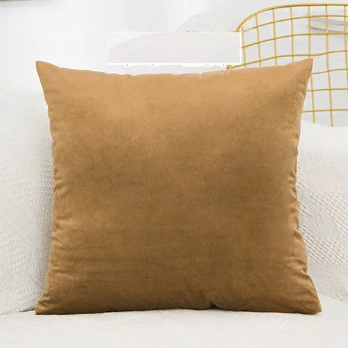 A solid velvet decorative cushion cover in a warm brown color resting on a white surface.