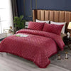 A luxurious quilted velvet bedspread in deep pink covers a bed with a padded headboard and white pillows.