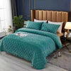 A teal quilted velvet bedspread with a fringed edge is displayed on a bed in a modern bedroom setting.