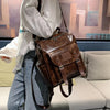 A woman wearing a white shirt and jeans is holding a brown PU leather fashion backpack.