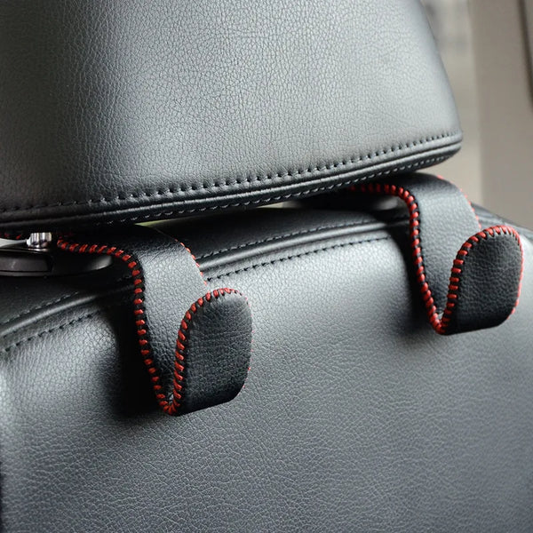 Close-up of black leather car seat headrest hooks with red stitching.
