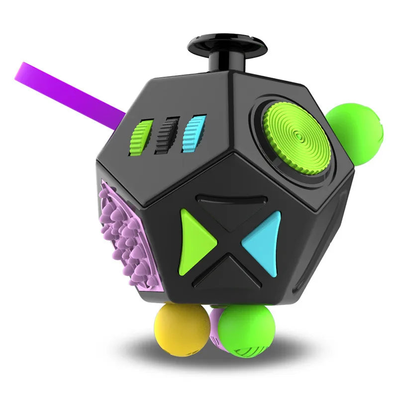 A black 12-sided fidget cube with green and blue accents and a purple stick, resting on a white surface.