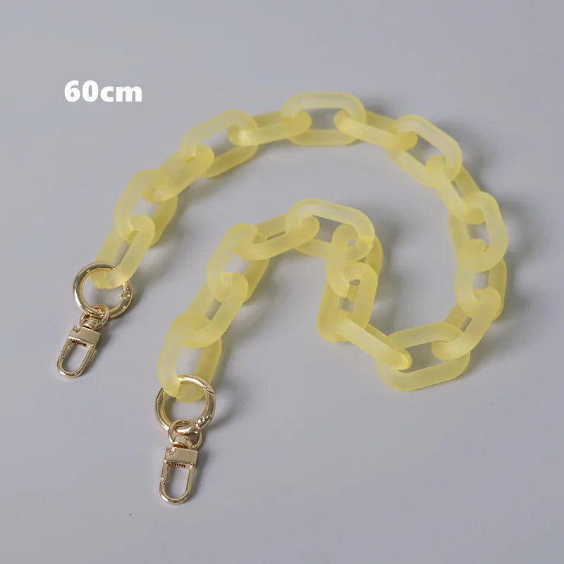 Helles gelbes abnehmbares Kettenriemen-Accessoire für eine Damenhandtasche, auf einer grauen Fläche ausgelegt.