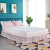 A white bed with a pink ruffled lace skirt and pillows in a bright room.