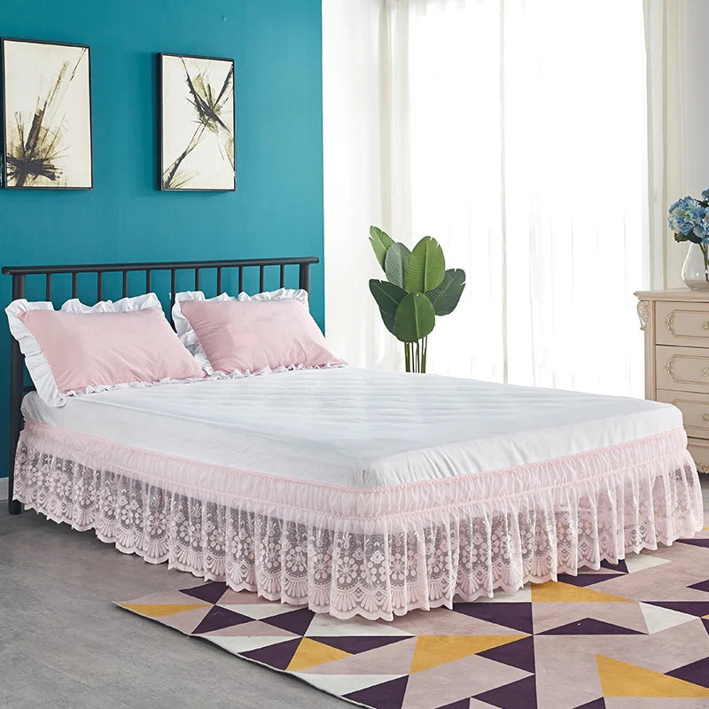 A white bed with a pink ruffled lace skirt and pillows in a bright room.