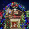 A house decorated with a large wreath of colorful string lights and festive holiday greenery at night.