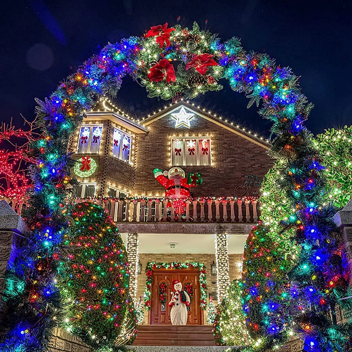 A house decorated with a large wreath of colorful string lights and festive holiday greenery at night.