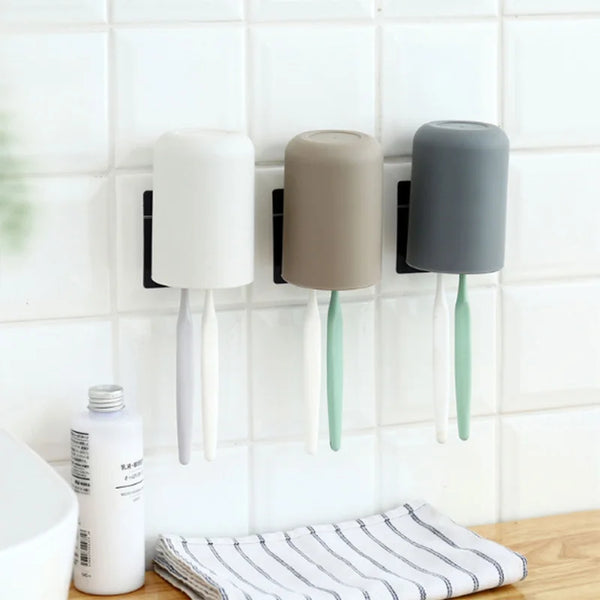 Wall-mounted toothbrush and cup holder with white, beige, and gray ceramic holders mounted on a white tiled wall.
