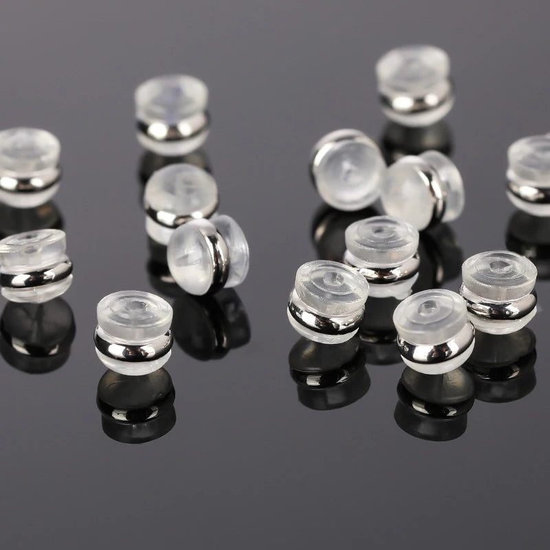 A collection of clear silicone rubber ear back stoppers with copper rings arranged on a dark reflective surface.