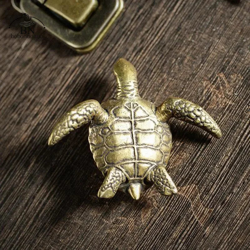 A small, antique-style solid copper turtle figurine resting on a dark wooden surface.