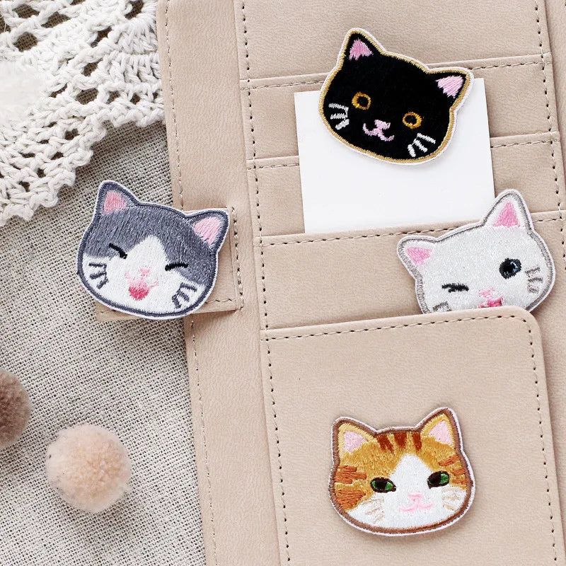 A collection of embroidered cat iron-on patches in black, gray, white, and orange on a beige leather pouch.