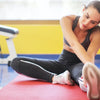 Eine Frau benutzt eine rote Yogamatte und einen externen Monitor im Fitnessstudio.