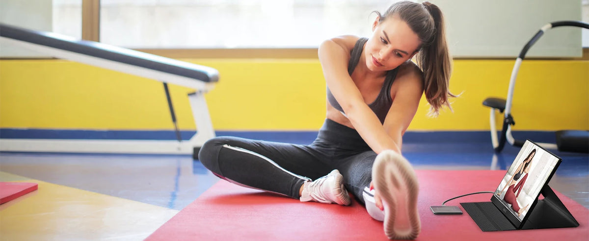 Eine Frau benutzt eine rote Yogamatte und einen externen Monitor im Fitnessstudio.