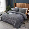 A gray quilted bedspread with a textured pattern is displayed on a bed in a modern bedroom setting.