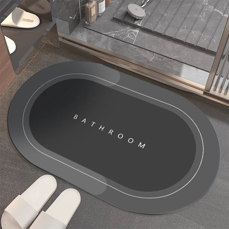 A dark gray bath mat with the word BATHROOM embossed on it, placed on a tiled floor.