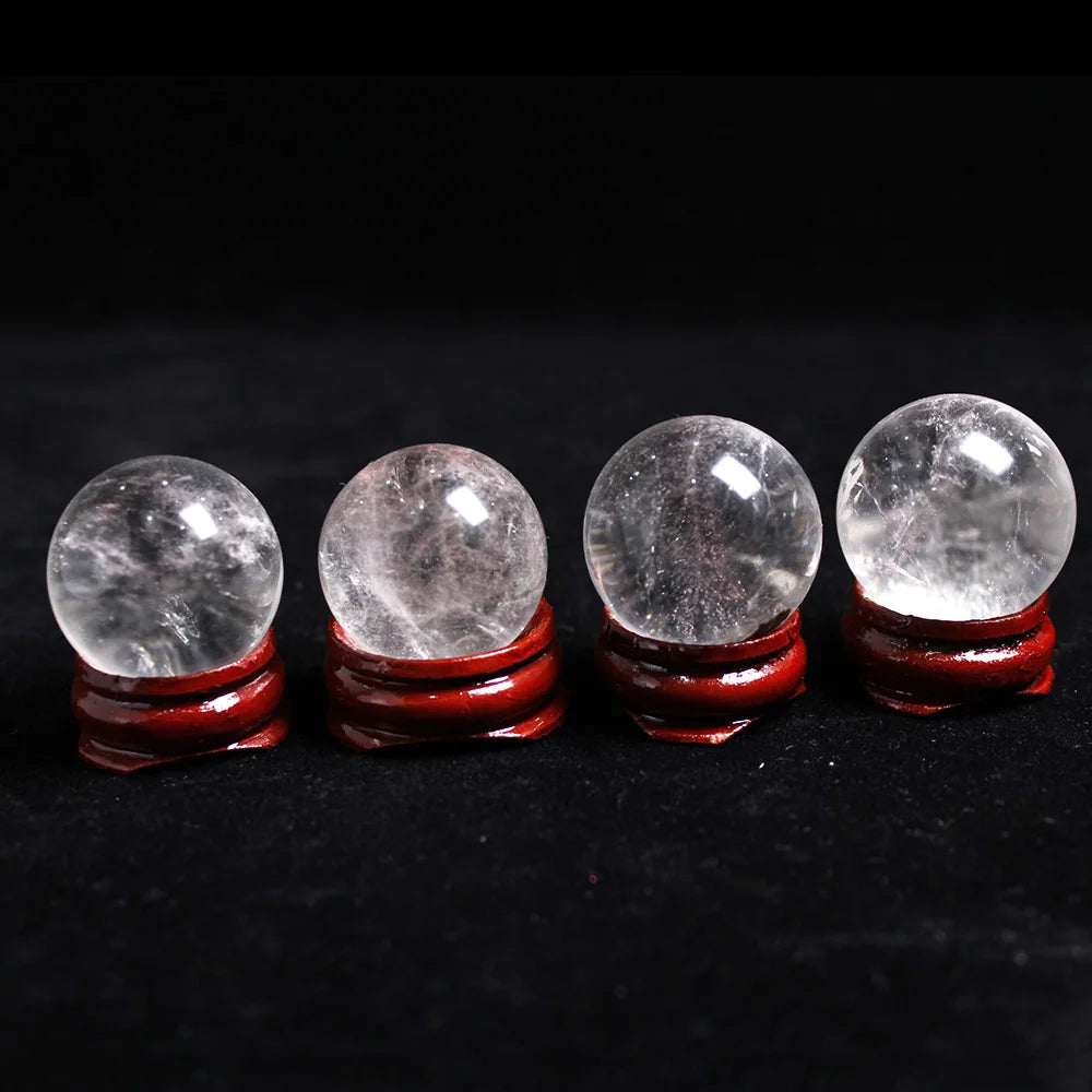 Four natural clear quartz crystal spheres set on a black surface.