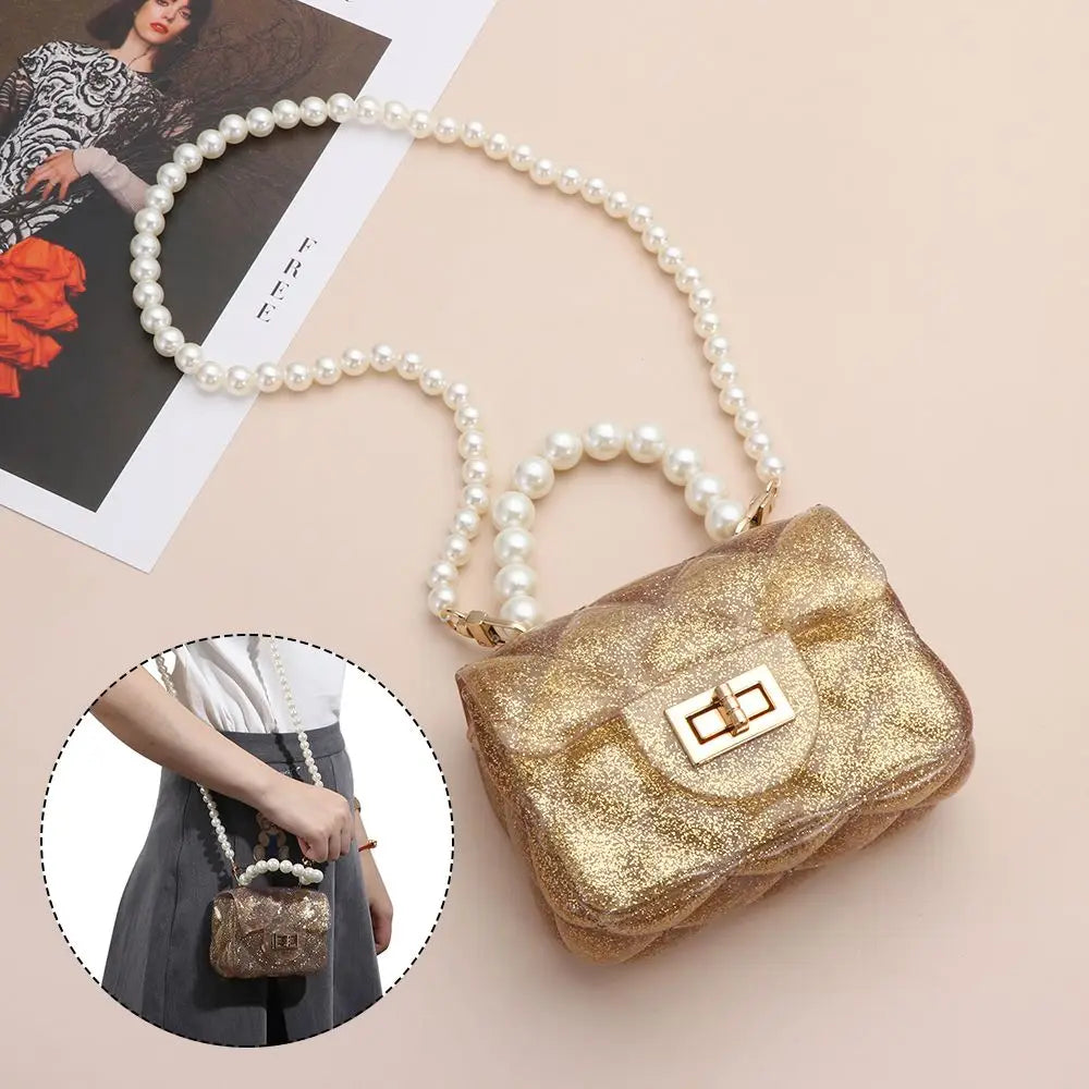 A golden glitter pouch bag is shown with a pearl chain strap, resting on a light pink background.
