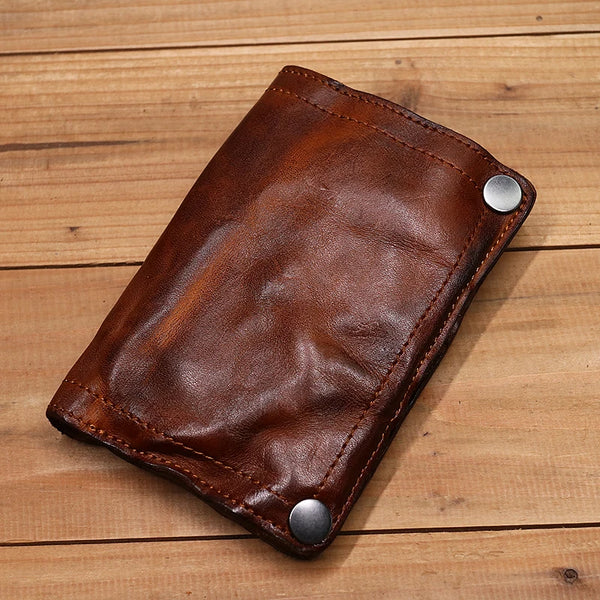 A brown genuine leather bifold wallet with stitching and silver snaps resting on a wooden surface.