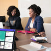 Vier Frauen arbeiten zusammen um einen Tisch mit Laptops und einem externen Monitor in einem Büro.