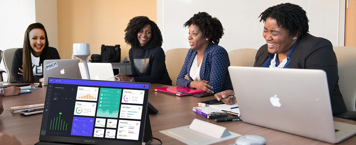 Vier Frauen arbeiten zusammen um einen Tisch mit Laptops und einem externen Monitor in einem Büro.
