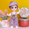 A purple-haired fashion doll wearing a lavender headband and overalls stands next to a pink plant and a round decorative obje