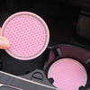A hand holds a pink, rhinestone-encrusted non-slip cup mat for cars inside a black storage compartment.