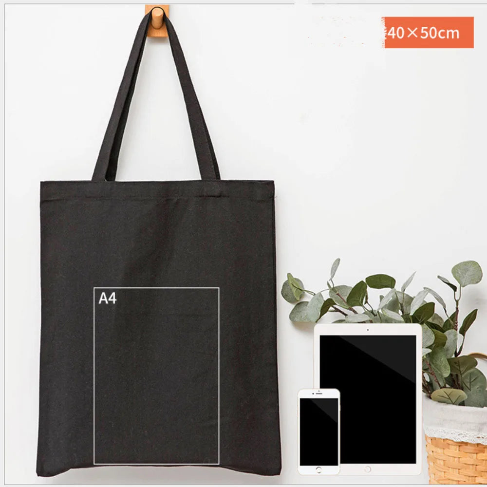 A black canvas tote bag with an A4 sized square printed on it, next to a smartphone and tablet.