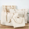 A row of beige canvas tote bags hanging against a white wall on a wooden surface.
