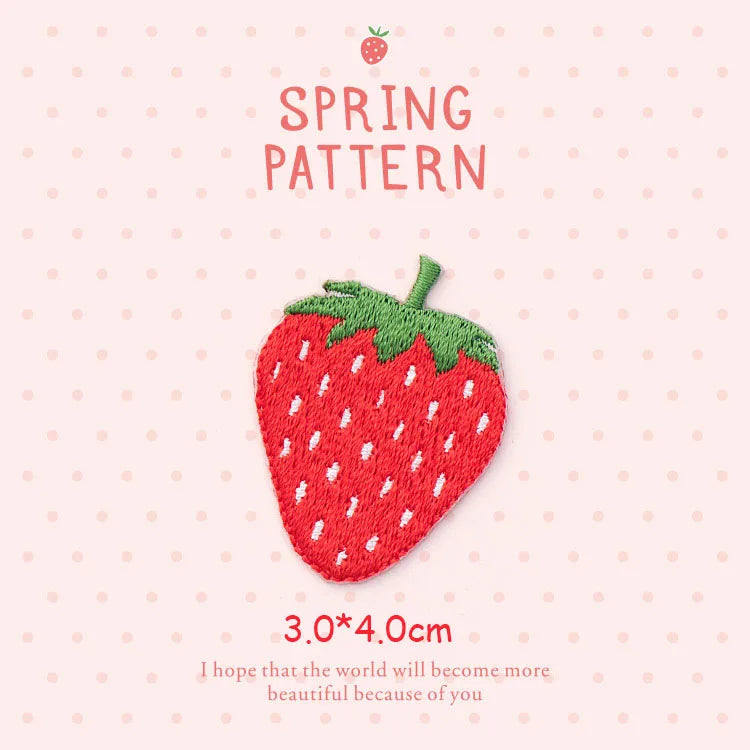 A pink strawberry embroidery patch with green leaves and white seeds on a light pink background.