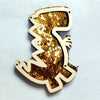 A wooden busy board piece shaped like a dinosaur, covered in gold and silver sequins.