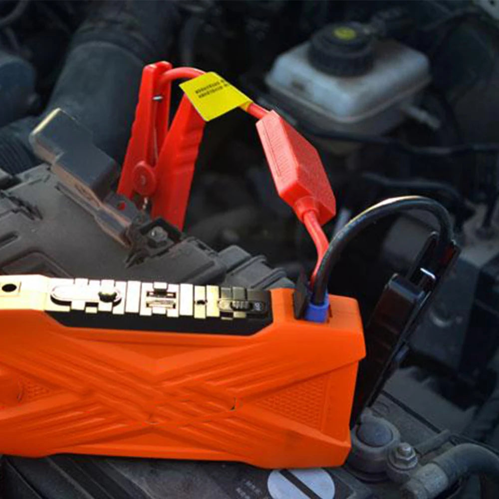 Orange jump starter clamps with red and yellow connectors attached to a vehicle battery