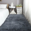 A fluffy gray Nordic fur rug placed on a bed with white linens and decorative elements.