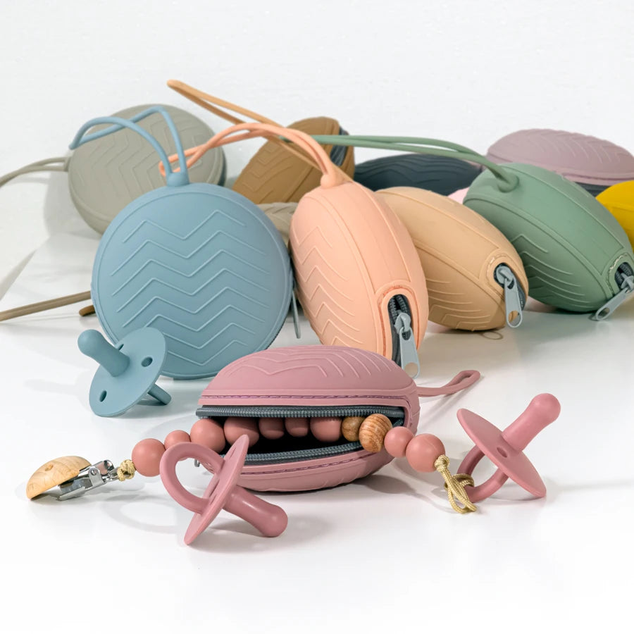 A collection of food-grade silicone pacifier cases in various pastel colors and textures arranged on a white surface.
