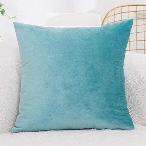 A solid teal velvet decorative cushion cover resting on a white sofa with a gold wire frame in the background.