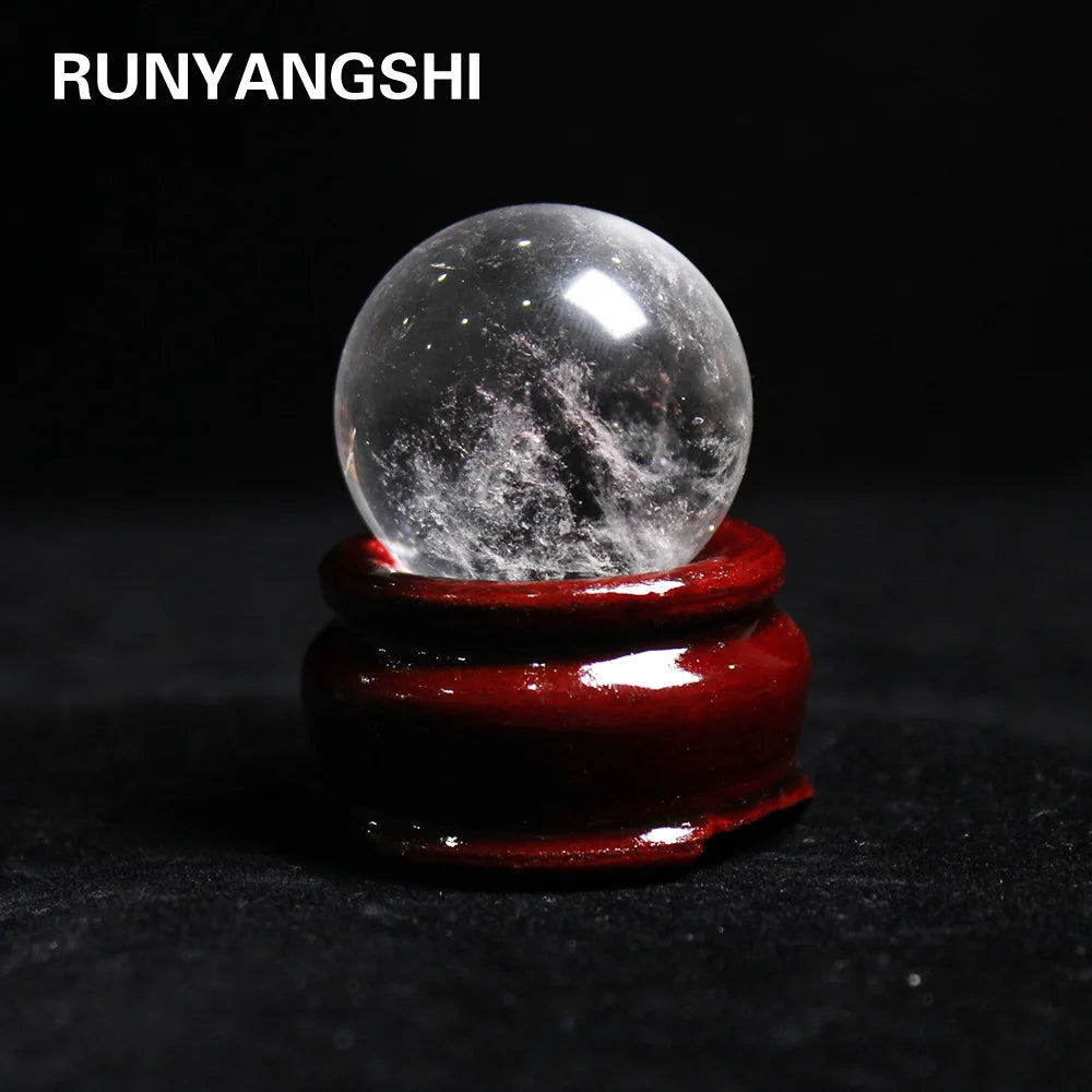 A clear quartz crystal sphere resting on a dark red wooden base.