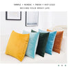 A collection of colorful velvet decorative cushion covers in yellow, teal, dark green, and burnt orange arranged on a white s