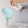 A hand is placing a white leaf-shaped suction cup soap onto a chrome faucet, with water flowing into a white sink.