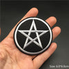A hand holds a black embroidered star symbol patch with white stitching on a dark background.