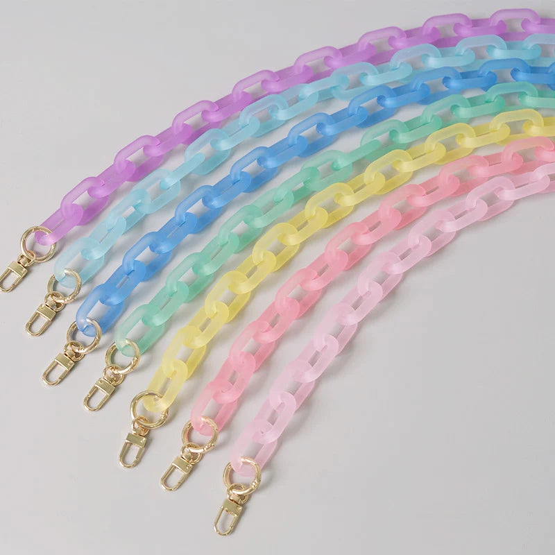 Eine Sammlung farbenfroher, irisierender Kettenriemen in einem Regenbogenverlauf auf grauem Hintergrund.