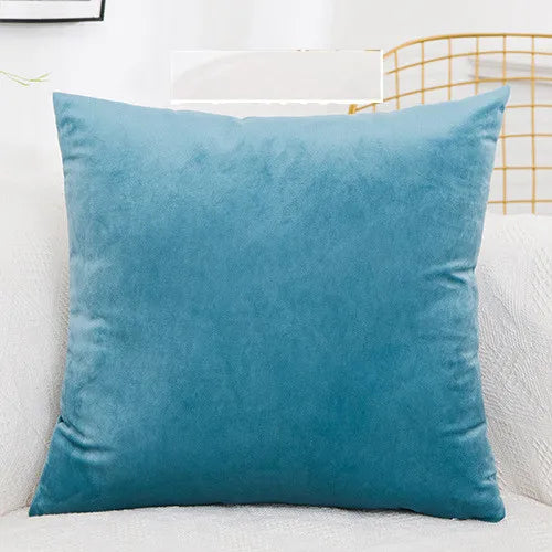 A solid teal velvet decorative cushion cover resting on a white sofa.