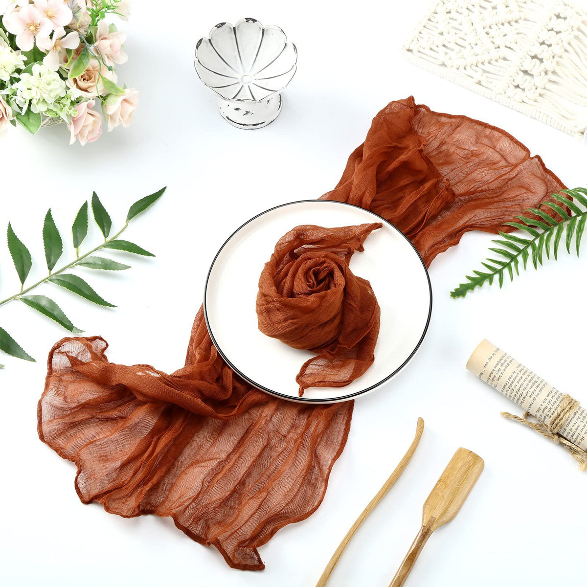 A brown cotton gauze table runner draped elegantly on a white plate with floral and greenery accents.