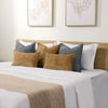 A collection of textured throw pillows in shades of beige, gray, and olive green on a white bed with modern framed art.