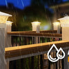 Outdoor solar post cap lights with warm LED illuminating a wooden fence and deck area.