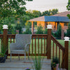 A wicker chair sits on a wooden deck with a brick fence and greenery in the background.