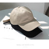 A beige baseball cap is shown resting on a black baseball cap on a white surface.