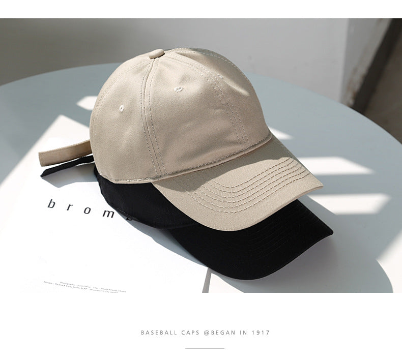 A beige baseball cap is shown resting on a black baseball cap on a white surface.