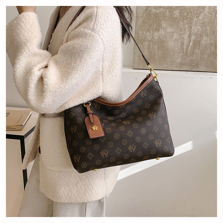 A woman holds a brown leather tote bag with a gold chain strap and a flap closure against a light background.