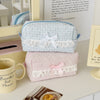 A light blue cosmetic pouch with white lace trim rests on a white surface next to a mug and a piece of food.